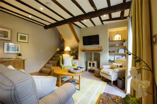 Beamed sitting room at The Bothy with wood-burning stove, staircase and tartan-check sofa