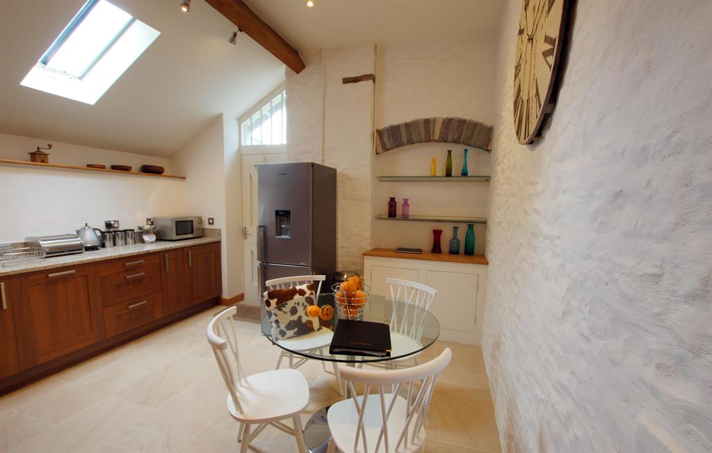 Alternative view of The Coach kitchen with skylit vaulted ceiling, exposed beam and round glass dining table