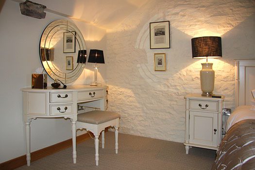 Elegant dressing area in The Laundry bedroom with antique dresser, oval mirror and framed prints