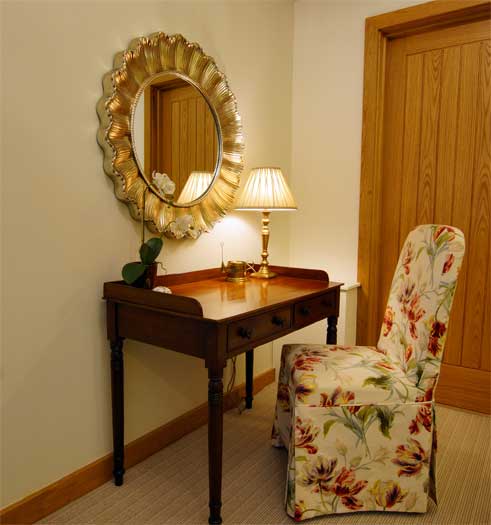 Antique dressing table with sunburst mirror and floral upholstered chair in The Dairy bedroom