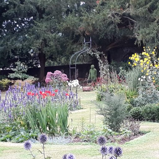 Herbaceous border in the Ty Mawr gardens with salvias, red poppies and rustic metal sculptures beneath mature yew trees