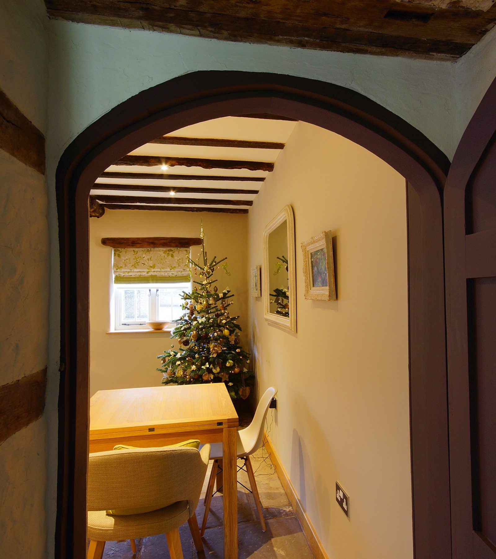 A festive Christmas tree glimpsed through the arched doorway of a beamed Ty Mawr cottage dining room