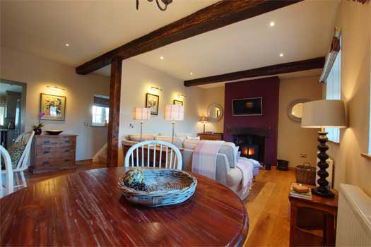 Dining area at The Cottage with round wooden table looking through to the sitting room and fireplace