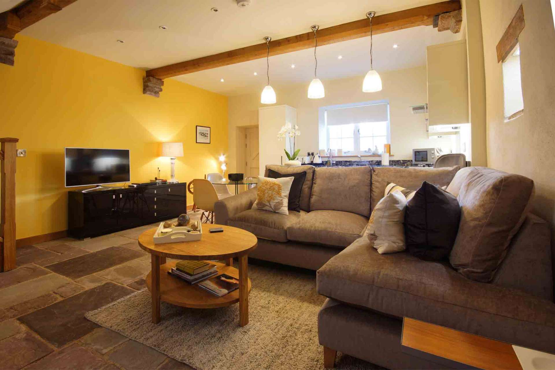 Open-plan living area at The Laundry with corner sofa, exposed beams and pendant lighting over the dining space