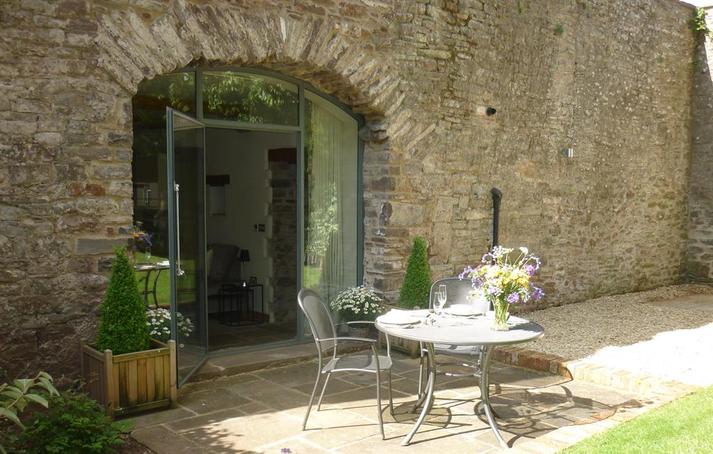 Private patio at The Laundry beneath the arched glass doorway with dining table and stone walls