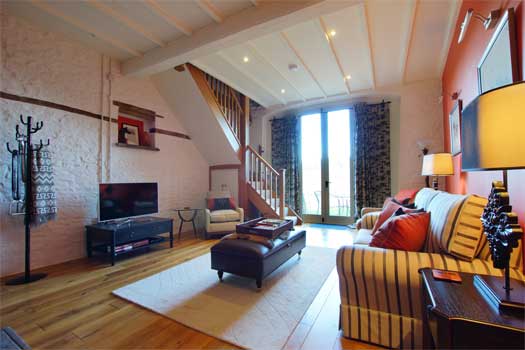 Vaulted living space at The Coach with exposed beams, staircase, wooden floors and French doors to the garden