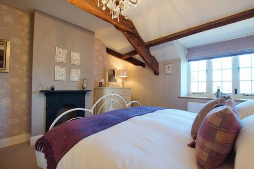 Romantic bedroom at The Cottage with wrought-iron bed, exposed beams and period fireplace