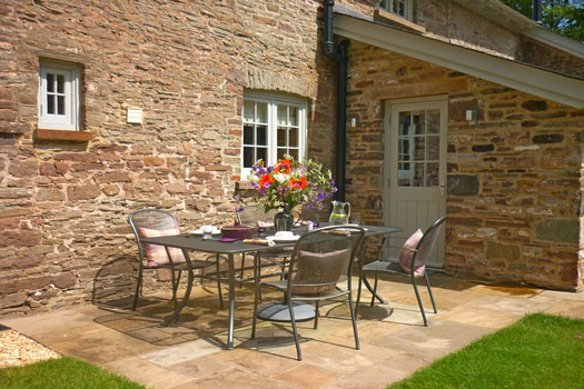 Private stone-flagged patio at The Cottage with dining table, chairs and fresh flowers set against traditional stone walls