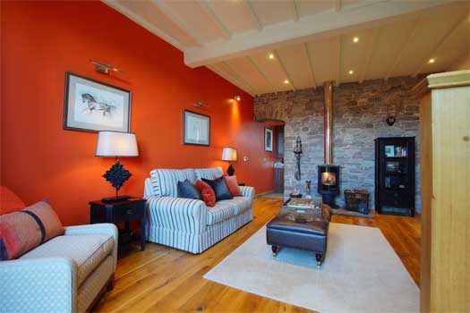 Living area at The Coach with striped sofas, deep terracotta walls and wood-burning stove against exposed stonework