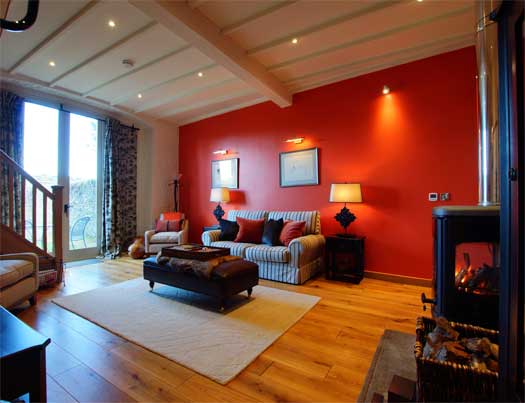 Cosy sitting area at The Coach with striped sofa, warm terracotta walls and a glowing wood-burning stove