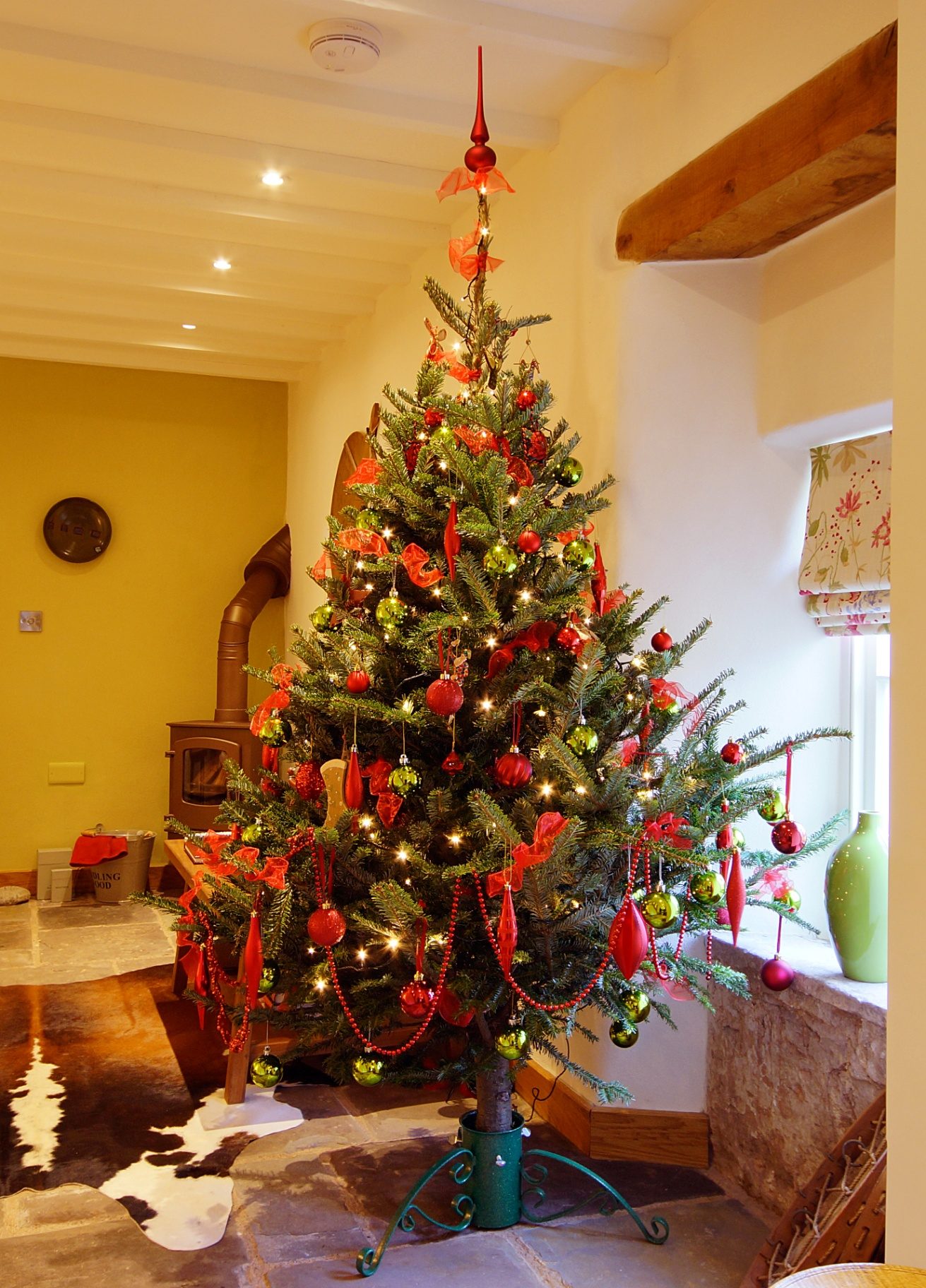 A Christmas tree hung with red and green baubles beside the wood-burning stove in a Ty Mawr cottage