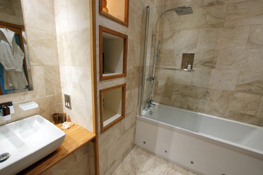 Marble-tiled bathroom at The Laundry with rainfall shower over the bath and inset shelving