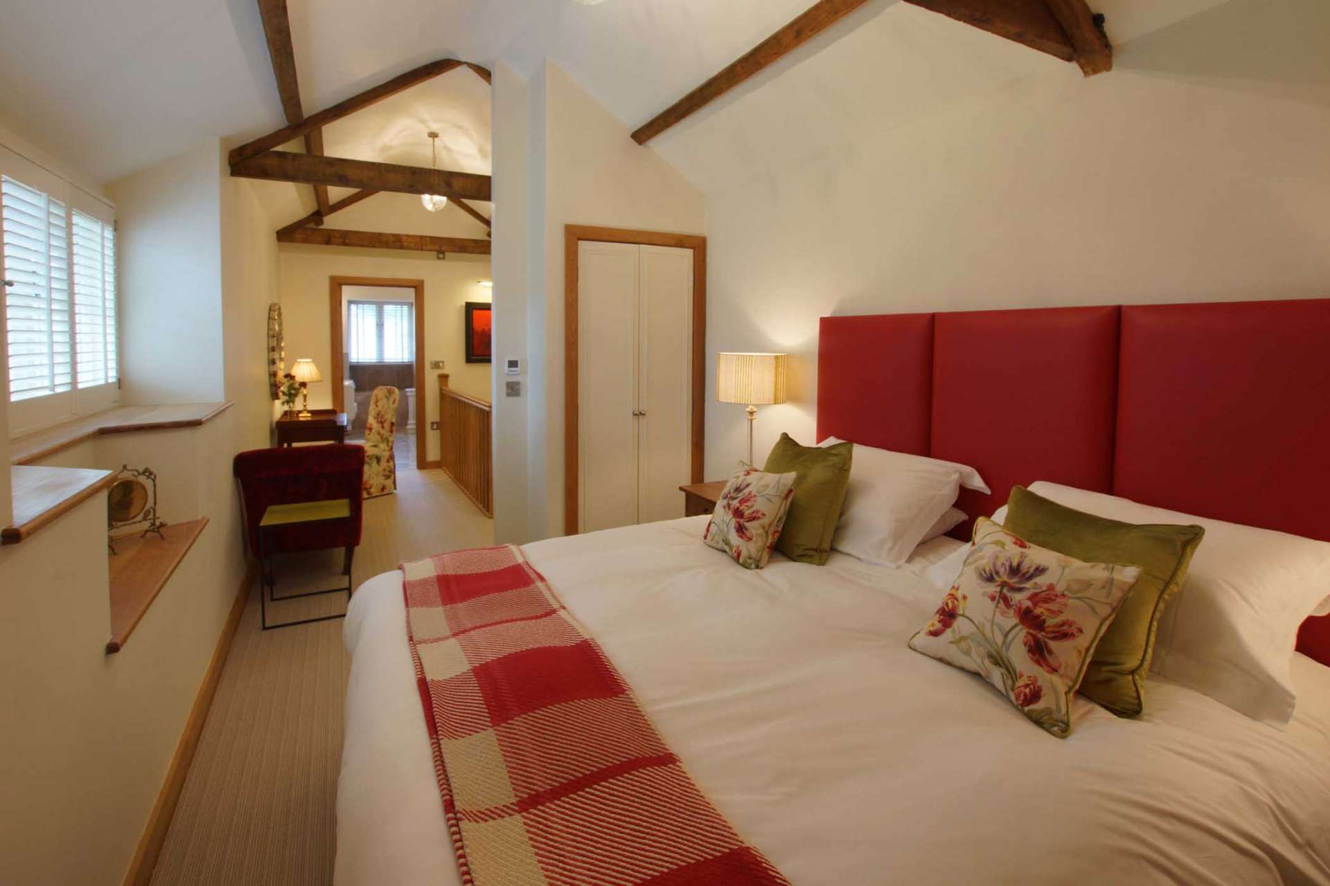 Vaulted bedroom at The Dairy with red headboard, exposed beam trusses and country textiles
