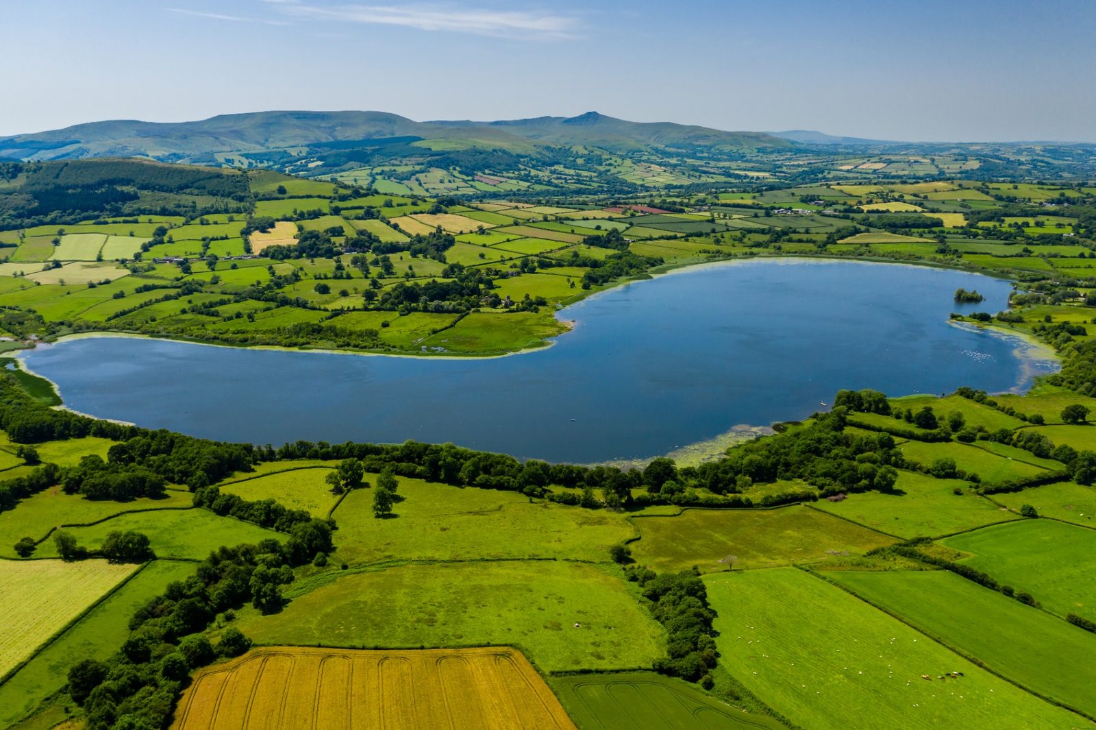 Aerial view over Llangorse Lake with the Brecon Beacons and Pen y Fan rising beyond patchwork fields