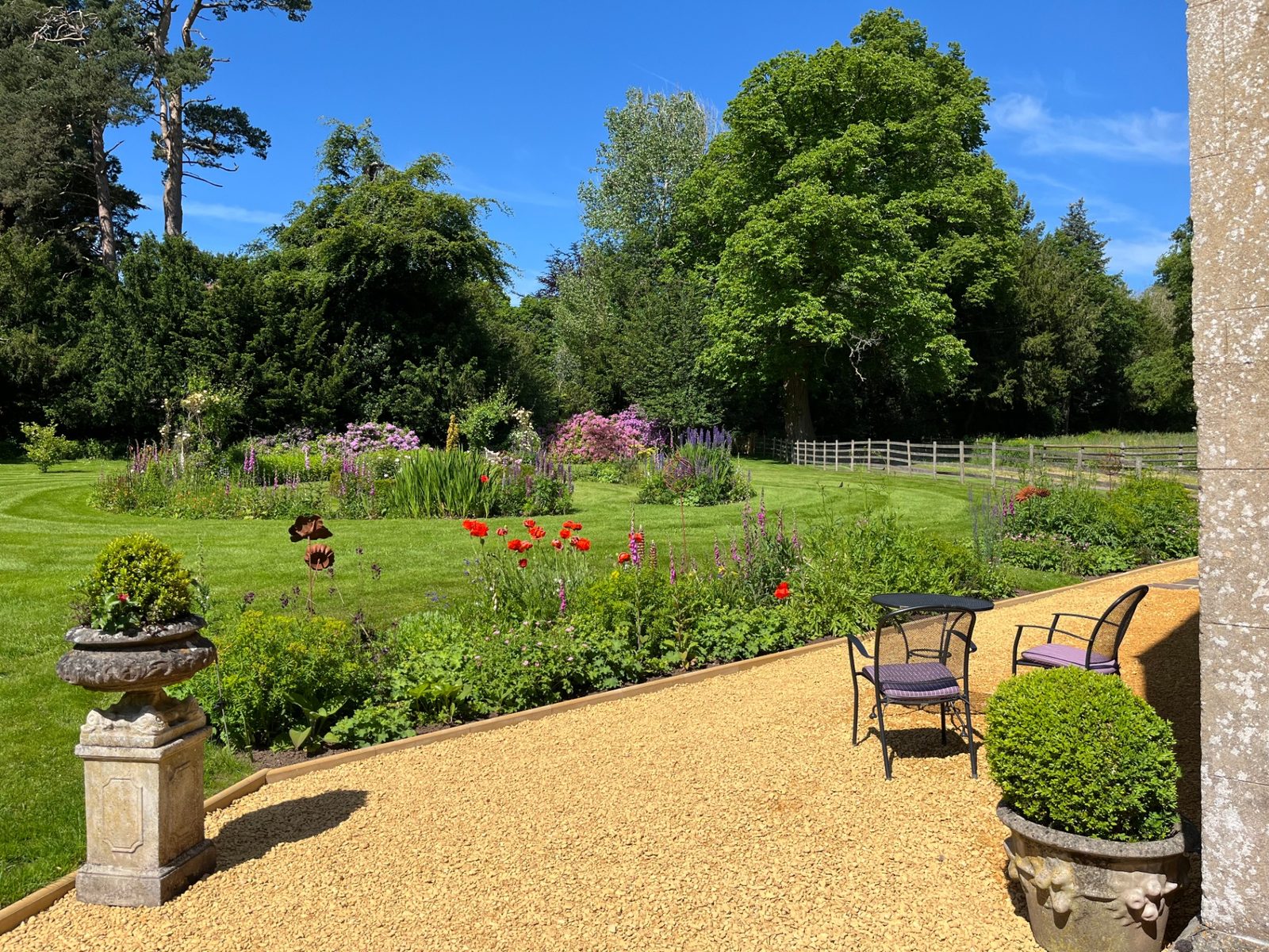 The Ty Mawr gardens in full summer bloom with lawn, flowering borders and mature specimen trees under a bright blue sky