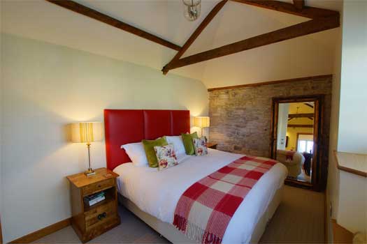 Super-king bedroom at The Dairy with red leather headboard, exposed beams and stone feature wall